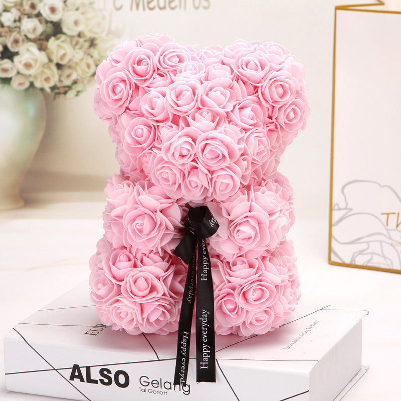 Ours créatif en roses roses avec un ruban noir, décor floral élégant posé sur des livres blancs.